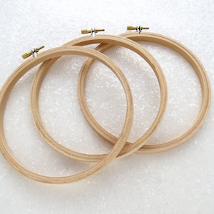 May include: Three wooden embroidery hoops of different sizes, with brass tightening screws. The hoops are nested together and are on a white background.