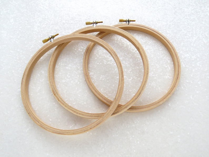 May include: Three wooden embroidery hoops of different sizes, with brass tightening screws. The hoops are nested together and are on a white background.