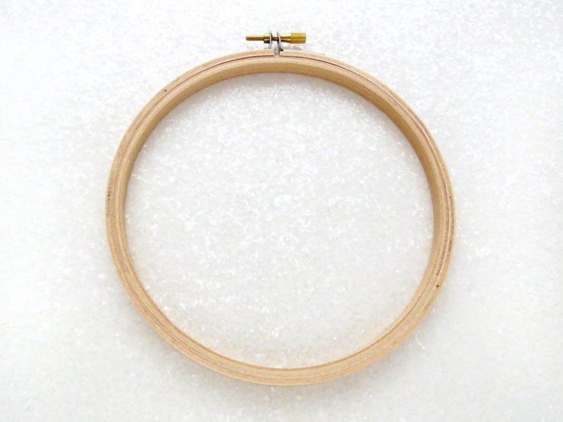 May include: A wooden embroidery hoop with a brass screw tightening mechanism. The hoop is round and has a natural wood finish.