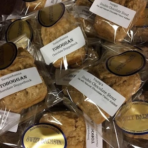 May include: A close-up of several individually packaged bakery items. The bakery items are labelled "Susquehanna Toboggan Chocolate Doppelbock" and "Young's Double Chocolate Stout Ale with Natural Chocolate Flavour Added". The bakery items are packaged in clear plastic bags with a white label that says "Sweet Barista" and a website address.