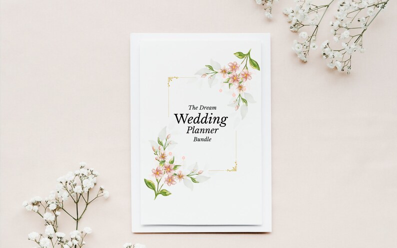 May include: A white wedding planner bundle with the text "The Dream Wedding Planner Bundle" in black. The planner is decorated with watercolor floral designs in pink, green, and gold. White flowers are in the background.