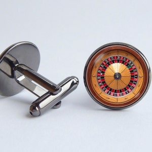 Può includere: Un paio di gemelli d'argento con un design a ruota della roulette nera e rossa. La ruota è incastonata in una cornice rotonda in legno.