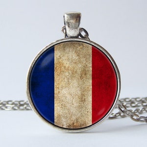 May include: A silver chain necklace with a round pendant featuring a distressed French flag design. The pendant is blue, white, and red.