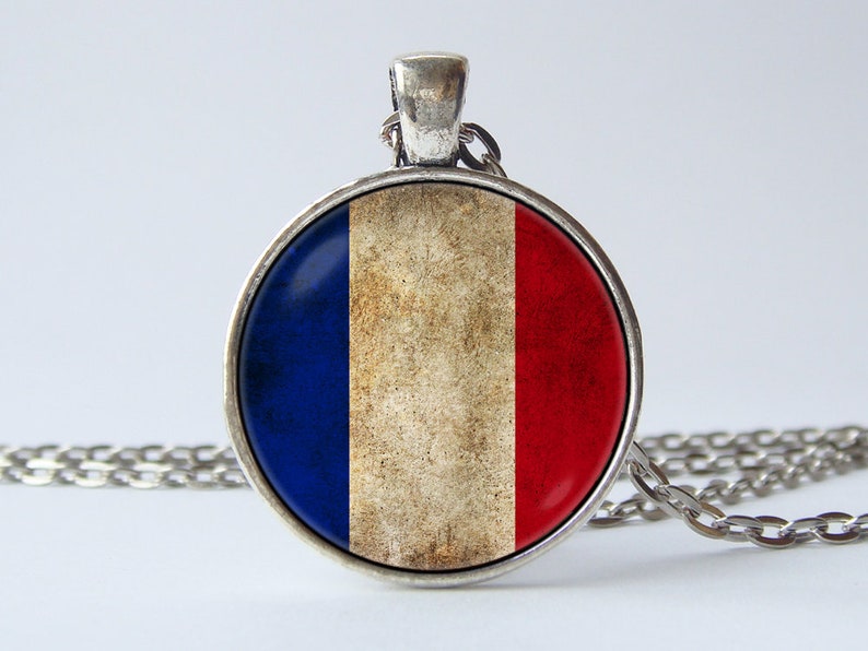 May include: A silver chain necklace with a round pendant featuring a distressed French flag design. The pendant is blue, white, and red.