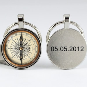 May include: A silver compass keychain with a detailed compass face and a date, "05.05.2012," engraved on the back. The compass face features directional markings and a needle. The keychain has a circular design.