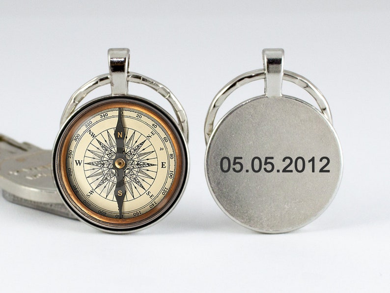May include: A silver compass keychain with a detailed compass face and a date, "05.05.2012," engraved on the back. The compass face features directional markings and a needle. The keychain has a circular design.