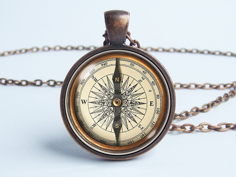 May include: Antique-style compass pendant necklace. The round pendant features a detailed compass rose design with directional markings and a needle. The pendant is encased in a bronze-colored metal frame and hangs from a matching chain.
