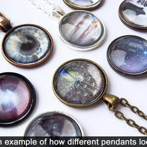 May include: A collection of different pendants with various designs, including an eye, a peacock feather, a galaxy, and a planet. The pendants are made of glass and are set in metal frames. The pendants are all on chains.