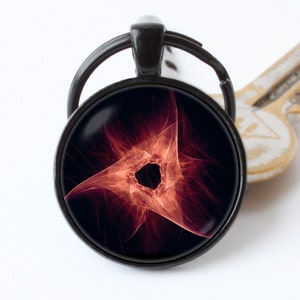 May include: A black metal keychain with a round glass charm featuring a red and orange abstract design. The design resembles a swirling vortex with a black center.