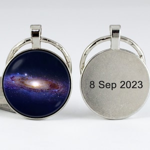 May include: A silver keychain with a round glass charm featuring a photo of the Milky Way galaxy. The back of the keychain has the date "8 Sep 2023" engraved on it.