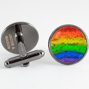 May include: A pair of black cufflinks with a rainbow design. The cufflinks are engraved with the text "JACOB & MASON".
