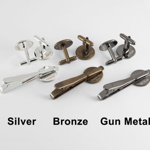 May include: Three sets of cufflinks and tie clips in silver, bronze, and gun metal. Each set features a round, engraved design with a date.