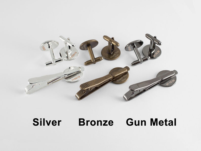 May include: Three sets of cufflinks and tie clips in silver, bronze, and gun metal. Each set features a round, engraved design with a date.