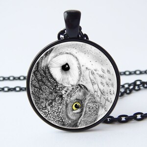 May include: A black chain necklace with a round glass pendant featuring a black and white yin yang design with two owl faces. The owls have yellow eyes.