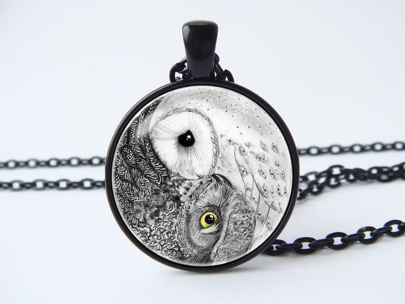 May include: A black chain necklace with a round glass pendant featuring a black and white yin yang design with two owl faces. The owls have yellow eyes.