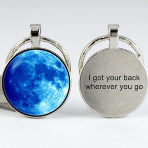 May include: A silver keychain with a blue moon image on one side and the text "I got your back wherever you go" on the other side.
