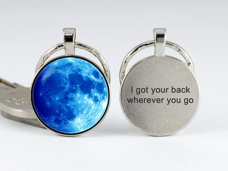 May include: A silver keychain with a blue moon image on one side and the text "I got your back wherever you go" on the other side.