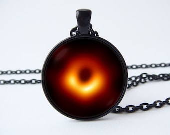 May include: Black chain necklace with a round glass pendant featuring a photo of a black hole with a bright orange ring.