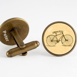 Puede incluir: Un par de gemelos de latón antiguo con un diseño de bicicleta vintage en un gemelo y el nombre "Peter" grabado en el otro gemelo.