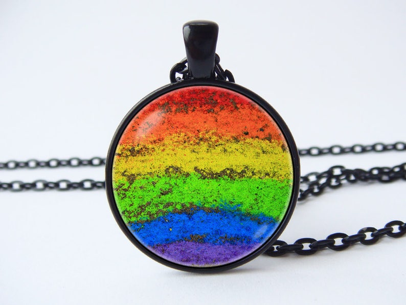 Puede incluir: Un collar con un colgante redondo de vidrio con los colores del arco&iacute;ris y una cadena negra. El colgante es redondo y tiene una superficie texturizada.