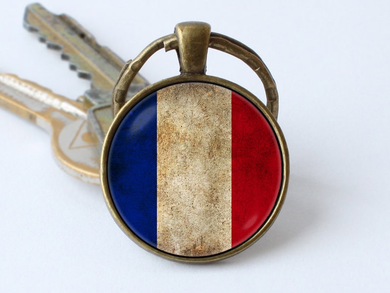 May include: A bronze key chain with a round glass charm featuring the French flag. The flag is distressed and has a vintage look.