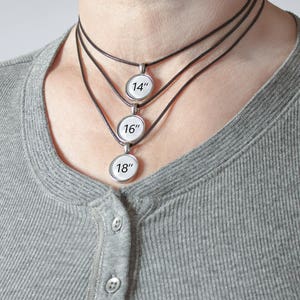 May include: Three black leather necklaces with silver round pendants. The pendants are labeled 14", 16", and 18".