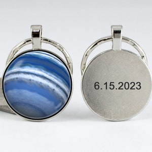 May include: A silver key chain with a round blue and white agate stone on one side and the date 6.15.2023 engraved on the other side.