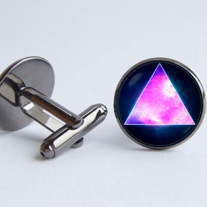 Puede incluir: Un par de gemelos con base de metal negro y parte superior redonda de vidrio. La parte superior de vidrio presenta un triángulo rosa y morado con un diseño de galaxia.