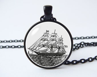 Op de afbeelding: Een zwarte ketting met een ronde glazen hanger met een zwart-witte lijntekening van een zeilschip.