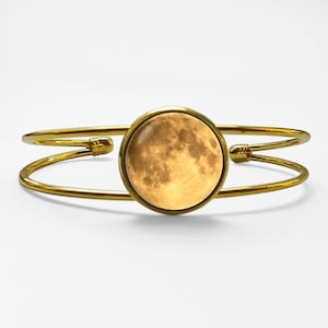 Peut inclure: Bracelet manchette doré avec un motif de lune circulaire. Le bracelet a un design à double bande avec une image de lune centrale, créant un accessoire sur le thème céleste. Un bijou élégant.