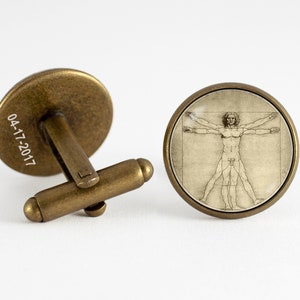 Peut inclure: Une paire de boutons de manchette avec une base en métal bronze et un dessus en dôme de verre. Le dôme de verre présente une image en noir et blanc de l'Homme de Vitruve, un célèbre dessin de Léonard de Vinci.