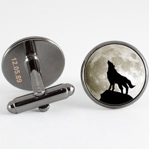 May include: A pair of silver cufflinks with a black and white image of a wolf howling at the moon. The back of one cufflink is engraved with the date "12.05.89".