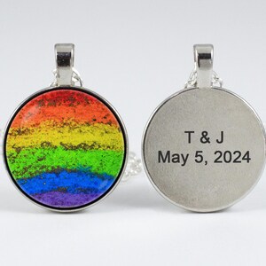 Puede incluir: Un collar de plata con un colgante redondo que presenta un dise&ntilde;o de arco&iacute;ris en un lado y el texto "T & J May 5, 2024" en el otro.