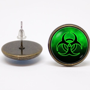 Peut inclure: Une paire de boucles d'oreilles avec un symbole de biohazard vert sur fond noir. Les boucles d'oreilles sont en métal et ont un fermoir à tige.