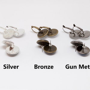 May include: Three pairs of earrings with different metal finishes: silver, bronze, and gunmetal. Each pair features a round, glass cabochon.
