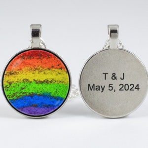 Puede incluir: Un collar de plata con un colgante redondo que presenta un diseño de arcoíris en un lado y el texto "T & J May 5, 2024" en el otro.