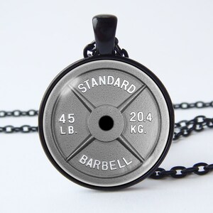 Puede incluir: Un collar de cadena negra con un colgante de placa de peso plateado. La placa tiene el texto "STANDARD BARBELL" y "45 LB. 20.4 KG."