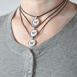 May include: Three silver pendant necklaces with black cords. The pendants are round and have the numbers 14, 16, and 18 printed on them.