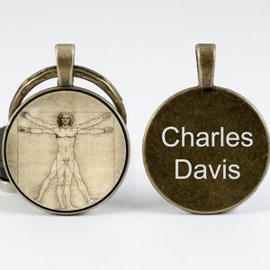 Puede incluir: Un llavero redondo de color bronce con una imagen detallada del Hombre de Vitruvio en un lado y el nombre "Charles Davis" grabado en el otro.