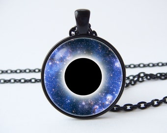 May include: Black necklace with a round pendant featuring a black hole surrounded by a blue galaxy with white stars.