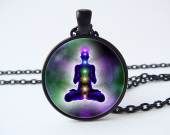 May include: A black chain necklace with a round glass pendant featuring a colorful image of a person in a yoga pose with seven chakras. The background is a swirling galaxy of green, purple, and white.