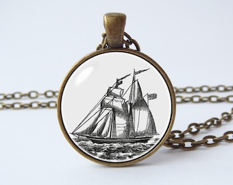 Op de afbeelding: Een bronzen ketting met een ronde glazen hanger met een zwart-witte lijntekening van een zeilschip.