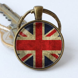 Puede incluir: Un llavero de bronce con un abalorio redondo de vidrio que presenta una bandera de la Union Jack de estilo vintage.