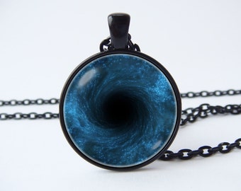 May include: A black pendant necklace featuring a circular pendant with a swirling blue and black design, resembling a galaxy or a black hole. The chain and pendant frame are black.