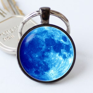 May include: A silver key chain with a round glass charm featuring a blue moon image.