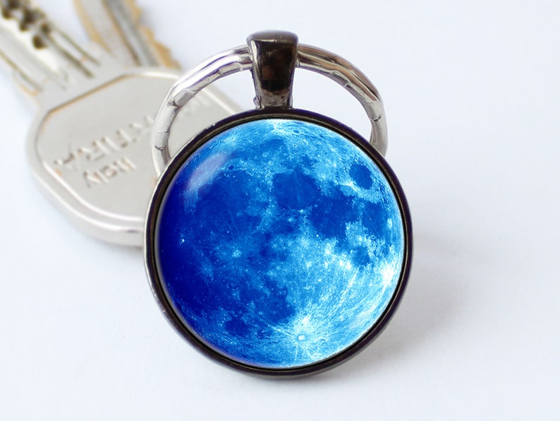May include: A silver key chain with a round glass charm featuring a blue moon image.