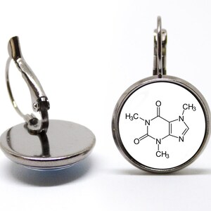 May include: Silver clip-on earrings with a white round charm featuring a black and white chemical structure diagram of caffeine.