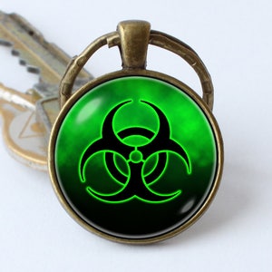 May include: A green and black biohazard symbol keychain. The symbol is on a round glass cabochon with a bronze metal frame.