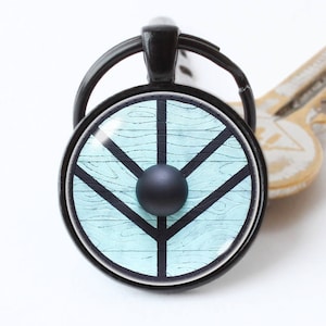 May include: A black key chain with a round, blue and white shield design. The shield has a black Y-shaped symbol in the centre.