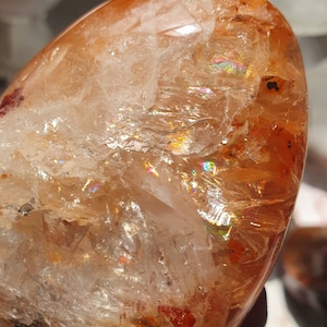 May include: A large, smooth, orange and white crystal with iridescent rainbow colors. The crystal is shaped like an egg.